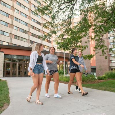 Students laughing and walking on the sidewalk on upper campus near Karlgaard Towers entrance.